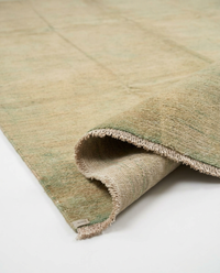 Close-up of sandy beige over-dyed wool rug texture with soft green undertones