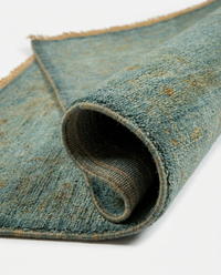 Close-up of teal blue over-dyed wool rug with golden-rust floral accents