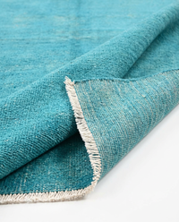 Turquoise over-dyed wool rug folded to show pile and border